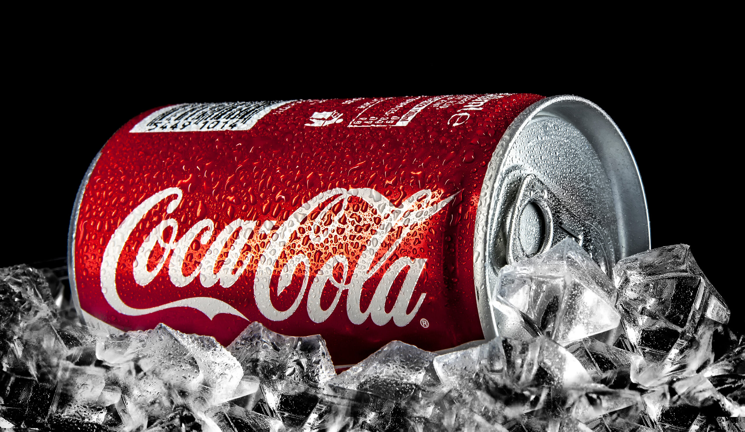 SWINDON, UK - FEBRUARY 2, 2014: Can of Coca-Cola on a bed of ice over a black background