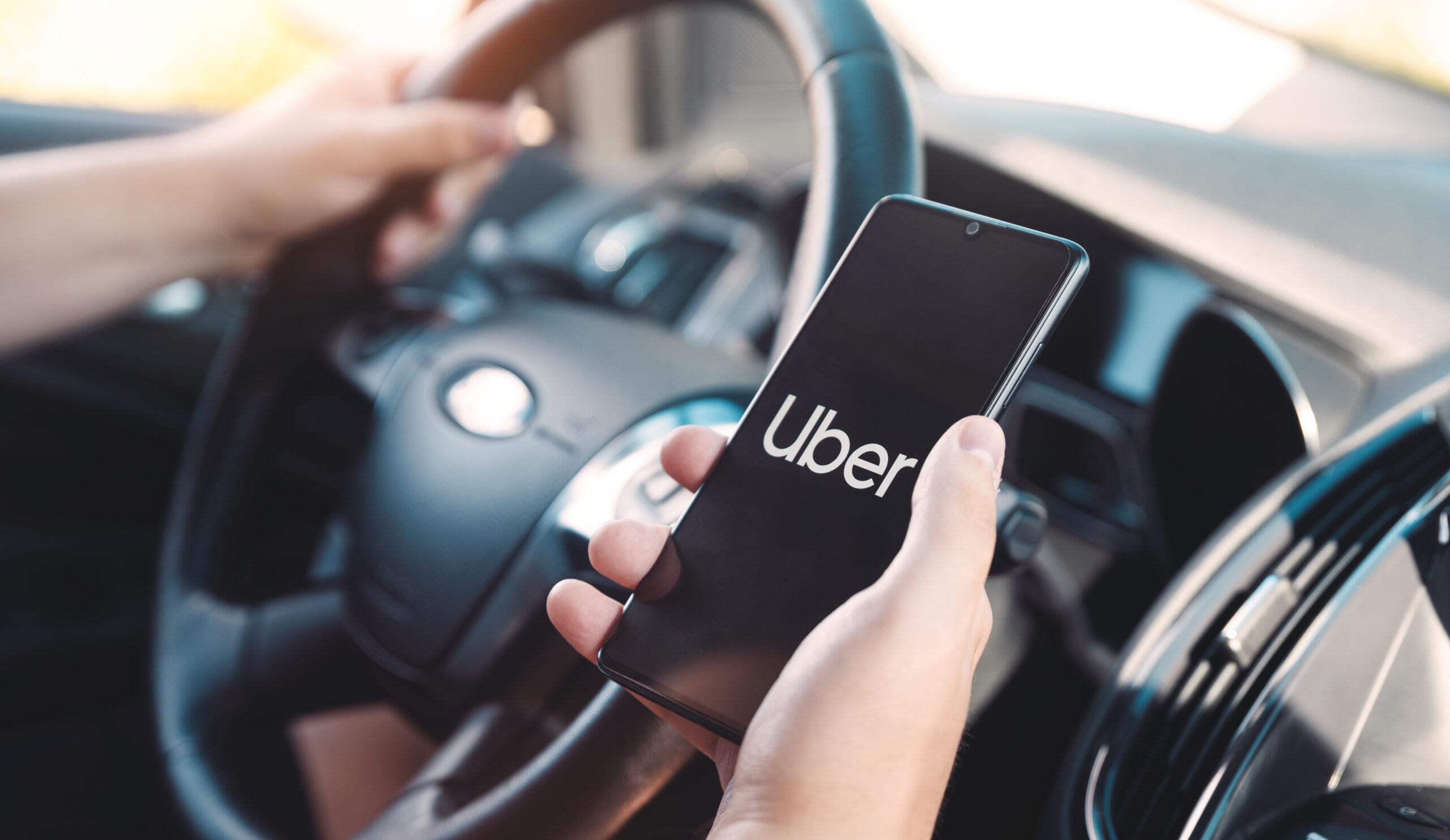 Wroclaw, Poland - AUG 25, 2020: Uber driver holding smartphone in car. Uber is sharing-economy service for ubran transport.