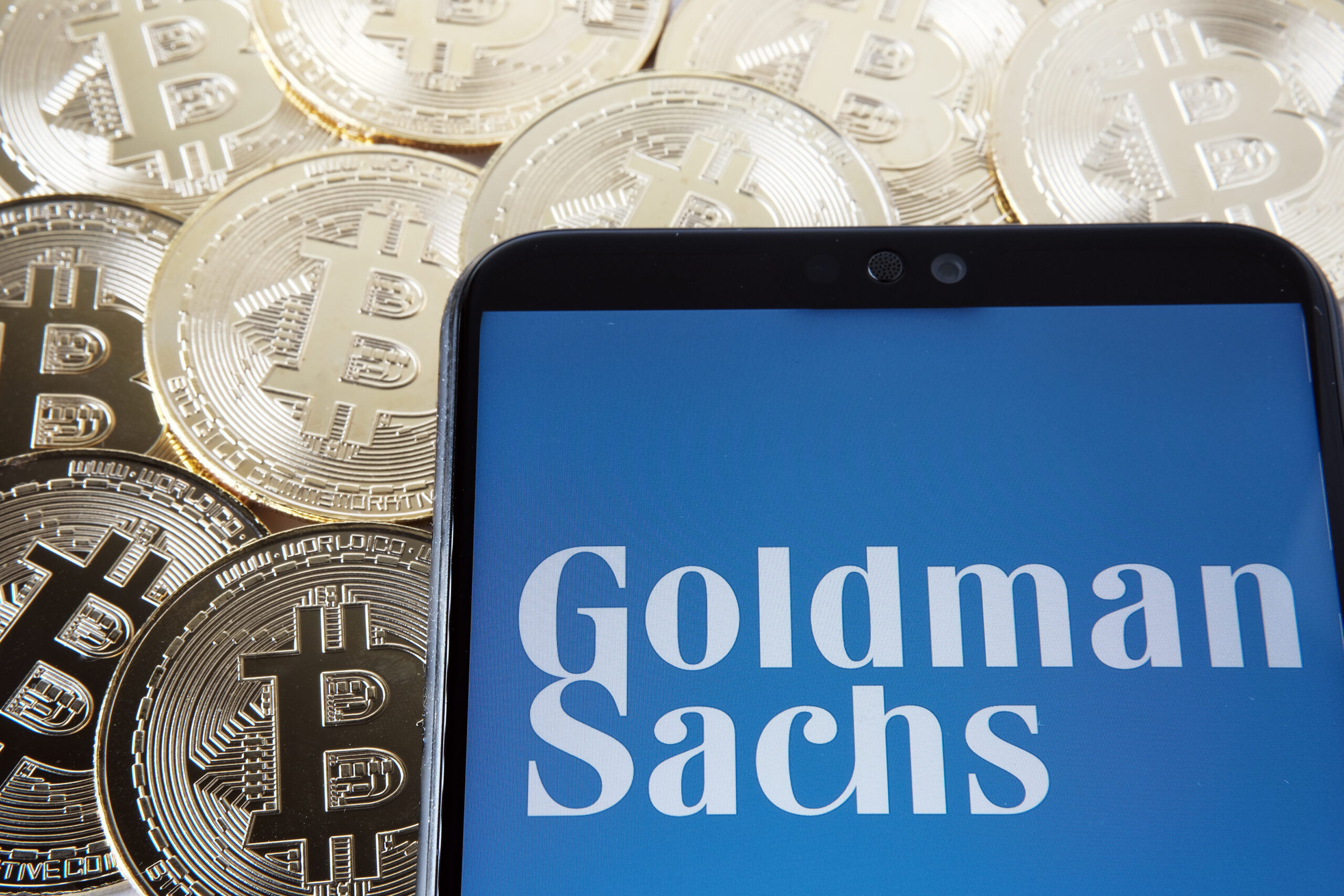 Goldman Sachs logo seen on the smartphone which is placed on the Bitcoin coins. Concept. Stafford, United Kingdom, April 7, 2021.