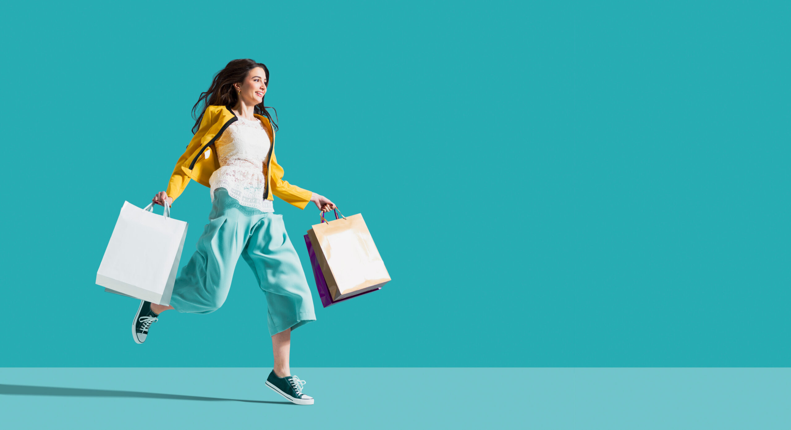 Cheerful happy woman enjoying shopping: she is carrying shopping bags and running to get the latest offers at the shopping center