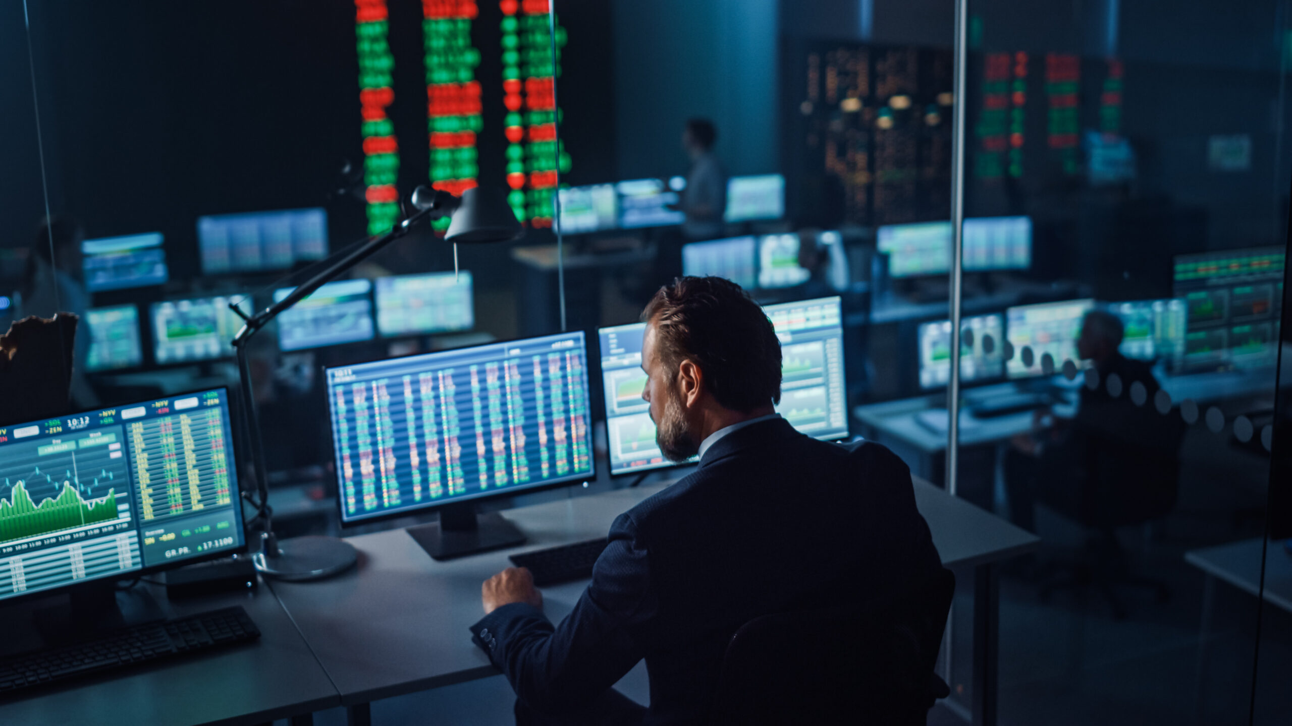 Professional Financial Data Analysts Working in a Modern Monitoring Office with Live Analytics Feed on a Big Digital Screen. Monitoring Room with Finance Specialists Sit in Front of Computers.