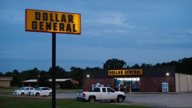 September 20, 2025, Sallisaw, Oklahoma. Dollar General store at twilight. Exterior of store and sign are lighted at dawn, vehicles in the parking lot, lights on inside. Propane tanks available outdoors. The rretail store chain is common in the region.