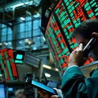 A stock trader works amidst flashing screens displaying market data, actively engaged in communication.