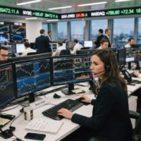 A busy trading floor with traders working on computers and monitors, displaying financial data and charts.